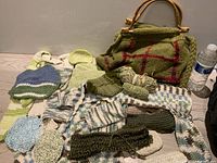 Full display of knitting bag, knitted slippers, various knitted garments, and skein of yarn alongside water bottle for scale