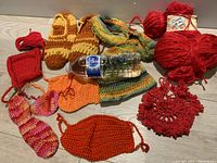 Various knitted and crocheted items alongside skeins of yarn. Items include slippers, a bag, swatches, face mask, and a loosely crocheted circular piece.