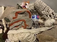 Photo showing multiple skeins of yarn in cream, brown, and orange colors along with some small knitted pieces and yarn remnants.