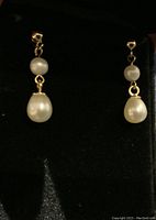 Pair of 14K yellow gold earrings each with a small round pearl on post and a larger teardrop pearl drop, placed on black velvet backing inside a jewelry box.