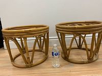 Pair of vintage MCM rattan stools side by side on wood floor with water bottle for scale