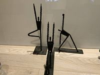 Photo showing three iron abstract figures placed on a wooden surface against a plain background, highlighting their forms and size.