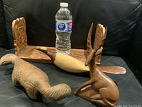 Photo showing all four carved wooden objects with a water bottle for scale, featuring the floral panel, bird, fish, and deer.