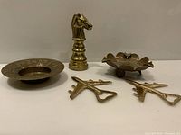 Front and angled view of all items showing three airplane-shaped bottle openers, chess knight shaped bottle opener, and two small brass bowls