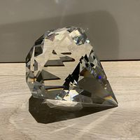 Clear diamond-shaped crystal paperweight positioned on side showing numerous facets and reflections.