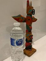 Front side view of colorful vintage wood totem pole next to a water bottle for size reference.