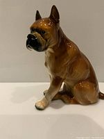 Front-left angle view of a glossy porcelain boxer dog figurine showing its seated pose and coloration.