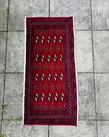 Top view of the rectangular red Turkmen backrest rug laid flat on concrete tiles, showing the full gul pattern design
