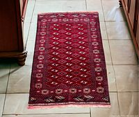 Full view of the Turkmen rug laid out on tile floor, showing the overall design and fringed ends.