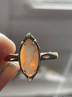 Close-up photo of the marquise-shaped orange cameo ring held between fingers showing the carved woman's profile relief.