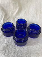 Four small cobalt blue glass jars without lids shown from above, arranged with openings visible.