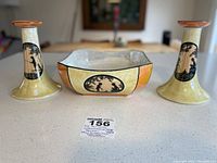 Front view of porcelain garniture set with square bowl and two candle holders on a white surface.