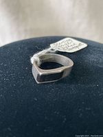 Sterling silver ring viewed from an angle showing the flat top with black rectangular onyx stone, resting on black fabric background, with visible artist tag.