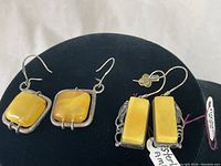 Two sets of vintage amber earrings mounted on black display. One set square amber in sterling silver, the other rectangular amber in ornate sterling silver frames.