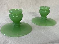 Two jadeite green glass candle holders placed on fabric background showing front and side views.