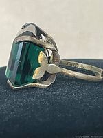 Side angled close-up of ring showing silver floral detail near the large green stone.
