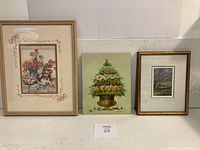 Three framed artworks shown together: bunny with flowers print in light wood frame, gold urn hand painting, and shepherd and flock watercolor in gold frame.