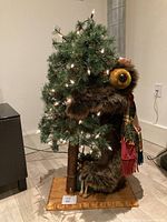 Full view of the bear hugging the Christmas tree figurine with lights, standing on wooden base.