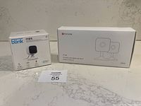 Blink Mini and Teckin TC100 indoor camera boxes on counter, showing they are new and boxed.