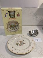 Royal Doulton Bunnykins 60th Anniversary ceramic mug and plate in original box, alongside pewter bowl and spoon and large Mikasa plate on white surface.