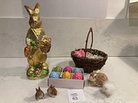 Photo showing foil-covered bunny, woven basket, six wood eggs, straw bunny, fluffy chick, and two resin bunnies arranged on a countertop.