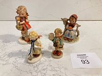 Four Hummel figurines displayed on marble surface showing the group