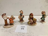 Four Hummel figurines arranged in a row on marble surface, clearly showing size and details