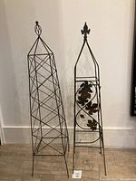 Two metal garden trellises side by side against wall, showing geometric wireframe trellis and leaf motif trellis.