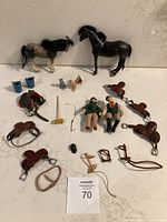 Overall view of two horse toys, rider dolls, animal figures, saddles, bridles, and small accessories arranged on white surface.