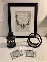 Photo showing the entire lot including the framed print, black lantern, metal decor piece, and four glass coasters arranged on a counter.