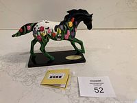 Side view of the painted pony figurine showing detailed tulip design and gold plaque on black base.
