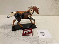 Front perspective of a collectible painted horse figurine on a black base with tag and card visible.