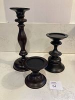 Three dark brown wood Pottery Barn candle holders of varying heights placed on a countertop. Shows overall set composition.