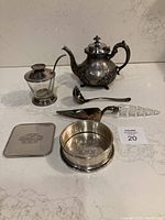 Photo showing all items in the set: teapot, jam jar, ladle, cake server, and two coasters on a marble surface.