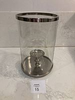 Full view of the glass and silver-colour metal hurricane lamp on a marble surface showing overall size and condition.