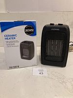 Black Likewise ceramic heater alongside its original box placed on a countertop.