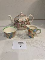 Set of teapot, creamer, and sugar bowl with seller's lot number card visible on counter