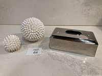 Wide view showing two white shell decor balls and a silver-tone rectangular tissue box cover on a marble surface.