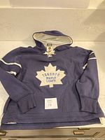 Front view of navy blue Toronto Maple Leafs hoodie with white maple leaf logo and text on chest, laid flat on surface