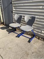 Pair of gray Pantoswing Lupo chairs with blue metal frames set outside against siding