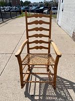 Front view of the rocking chair showing six ladder back wooden slats, curved armrests, and woven seat construction.