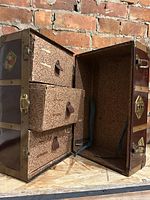 Side view with trunk lid open revealing three interior drawers covered with patterned paper and leather pulls, and interior lining with floral/geometric pattern.