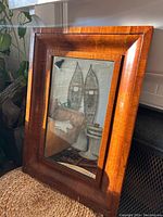Overall view of antique Empire style rectangular mirror leaning on woven surface with visible figured maple wood grain and original mirror reflective surface.