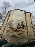 Front-side view showing hand-painted landscape with trees and shoreline on translucent early plastic panel, damage visible on gimp trim.