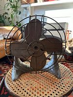 Front of a Canadian made Art Deco Catamaran electric fan showing metal three-blade propeller with wire cage and curved base.