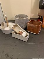 Photo showing six assorted plant pots and planters: large gray round planter, square terracotta planter, white rectangular planters, and a white hanging planter with wooden handle.