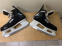 Pair of Bauer Charger ice hockey skates, side view showing black synthetic material, white blade holders, and metal blades.
