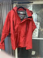 Red Burton Ak snowboard/ski jacket hanging, showing full front with red outer shell and zipped pockets