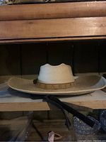 Side profile of light tan woven straw sombrero with decorated leather band and black chin strap, showing form and detail.