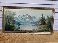 Front overview of framed landscape lithograph leaning against a white wall on a brown carpet